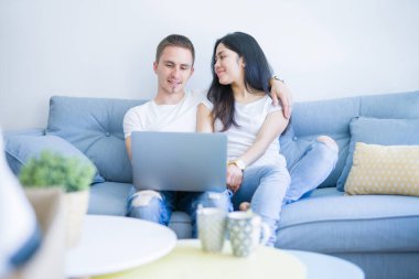 Karton kutular etrafında yeni evde dizüstü bilgisayar kullanarak kanepede oturan genç güzel çift