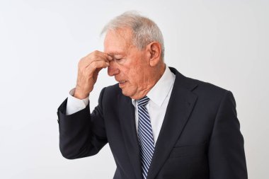 İzole edilmiş beyaz arka planda duran takım elbiseli kıdemli gri saçlı işadamı yorgun argın burnu ve gözleri ovuşturup yorgunluk ve baş ağrısı hissediyor. Stres ve hüsran kavramı.