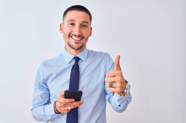 Genç yakışıklı iş adamı, izole edilmiş arka planda akıllı telefon kullanıyor. Gülümsüyor ve gülümsüyor. İşaret veriyor.