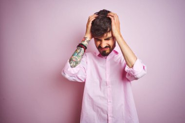 Dövme giyen genç adam izole pembe arka plan üzerinde duran baş ağrısı umutsuz acı ve stresli çünkü ağrı ve migren. Eller baş üstünde.