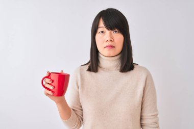 Genç, güzel bir Çinli kadın izole edilmiş beyaz arka planda kırmızı kahve içiyor. Akıllı bir yüz ifadesiyle ciddi ciddi düşünüyor.