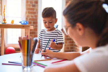 Güzel öğretmen ve çocuk anaokulunda renkli kalemlerle resim çiziyor.