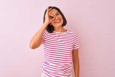 İzole pembe arka plan üzerinde duran çizgili t-shirt giyen genç güzel kadın el gülümseyerek ok jest yapıyor, mutlu yüz ile parmaklardan bakan göz.