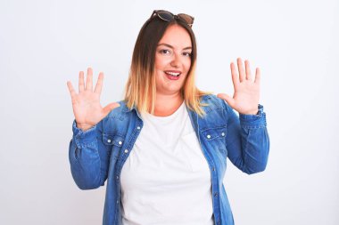 İzole edilmiş beyaz arka plan üzerinde duran kot gömlek giyen güzel bir kadın on numarayı gösterip işaret ederken kendinden emin ve mutlu bir şekilde gülümsüyor..