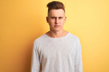 İzole edilmiş sarı arka plan kuşkucu ve gergin beyaz tişörtlü genç yakışıklı adam sorun yüzünden üzgün. Negatif kişi.