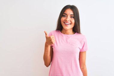 İzole edilmiş beyaz arka plan üzerinde duran pembe günlük tişört giyen genç ve güzel bir kadın mutlu bir el hareketi yapıyor. Kameraya bakıp başarıyı gösteren ifade onaylanıyor.