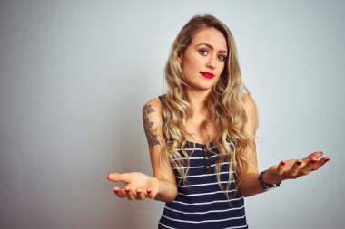 Çizgili tişört giyen genç bir kadın beyaz izole edilmiş arka planda duruyor. Hiçbir fikri yok ve kolları açık, hiçbir fikri yok..