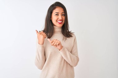 Balıkçı yaka kazak giyen güzel Çinli kadın izole edilmiş beyaz arka planda duruyor. Arka tarafı işaret ediyor. El ve baş parmakları havada, kendine güvenen.