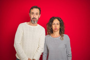 Güzel bir orta yaşlı çift, izole edilmiş kırmızı arka plan yanaklarına süveter giyip komik suratlarıyla tüttürüyorlar. Havayla şişmiş ağız, çılgın bir ifade..