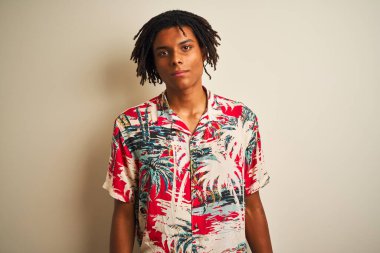 Tatilde saçı rastalı Afro bir adam. Yüzünde ciddi bir ifadeyle izole edilmiş beyaz bir arka plan üzerinde yazlık tişört giyiyor. Basit ve doğal bir şekilde kameraya bakıyorsun..