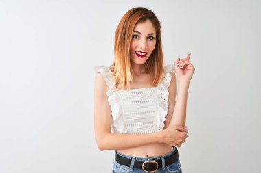 Güzel kızıl saçlı kadın yüzünde büyük bir gülümseme ile izole beyaz arka plan üzerinde duran rahat t-shirt giyen, kameraya bakarak yan el ve parmak ile işaret.