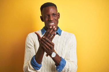 İzole edilmiş sarı arka planda kot ve beyaz kazak giyen Afro-Amerikalı bir adam. Ellerinde ve parmaklarında ağrı, iltihaplanma.