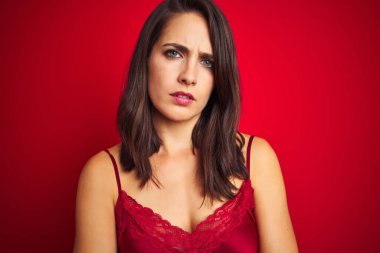 Genç ve güzel bir kadın kırmızı izole edilmiş arka plan üzerine seksi iç çamaşırı giyiyor şüpheci ve gergin, yüzünde çapraz kollu tasvip etmeyen bir ifade var. Negatif kişi.
