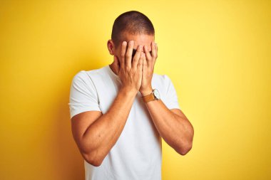 Sarı arka plan üzerine günlük beyaz tişört giyen genç beyaz bir adam ve ağlarken suratını ellerle kapatan üzgün bir ifade. Depresyon kavramı.