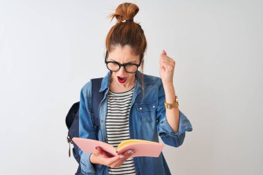 Sırt çantası giyen kızıl saçlı bir kadın izole edilmiş beyaz arka plan üzerine kitap okuyor öfkeyle bağırıyor, deliriyor ve el kaldırarak bağırıyor. Öfke kavramı.