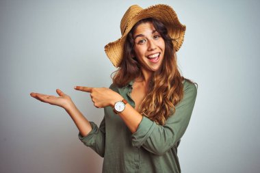 Yeşil gömlekli, şapkalı, beyaz arka planda genç ve güzel bir kadın kameraya hayret ediyor ve gülümsüyor..