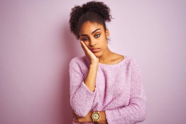 Kış süveteri giyen genç Afro-Amerikalı kadın izole edilmiş pembe arka planda duruyor. Kollarını kavuşturup depresyondan sıkılmış ve yorgun görünüyor..