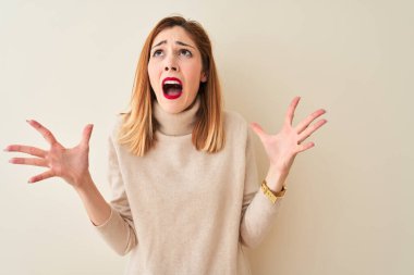 Kırmızı saçlı kadın, zarif balıkçı yaka kazak giyiyor. İzole edilmiş beyaz arka plan üzerinde duruyor. Deli gibi bağırıyor, agresif bir ifadeyle bağırıyor ve kollarını kaldırıyor. Hayal kırıklığı konsepti.