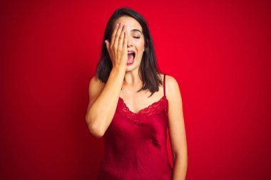 Genç ve güzel bir kadın, kırmızı iç çamaşırları üzerine seksi iç çamaşırları giyip bir gözünü elinle kapatıyor, yüzünde kendine güvenen bir gülümseme ve sürpriz bir duygu oluşuyor..