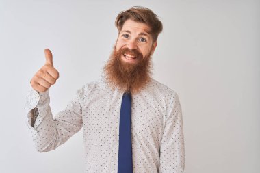 Genç kızıl saçlı İrlandalı işadamı, soyutlanmış beyaz arka planda duruyor. Gururlu görünüyor, gülümsüyor, baş parmak işareti yapıyor.