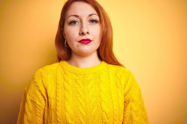 Kışlık süveter giyen genç bir kadın izole edilmiş sarı arka planda duruyor ve yüzünde ciddi bir ifade var. Basit ve doğal bir şekilde kameraya bakıyorsun..