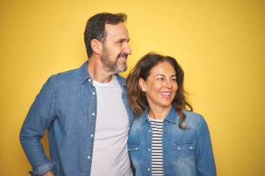 Güzel, orta yaşlı bir çift, izole edilmiş sarı arka plan üzerinde kot tişört giyiyorlar. Yüzlerinde gülümseme, doğal bir ifade ile yan yana bakıyorlar. Kendinden emin gülen.