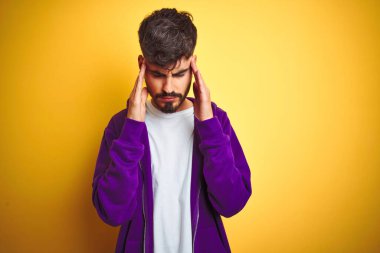 İzole edilmiş sarı arka plan üzerine spor mor kazak giyen genç bir adam. Başı ağrıyan bir adam. Stres yüzünden. Migren ağrısı..
