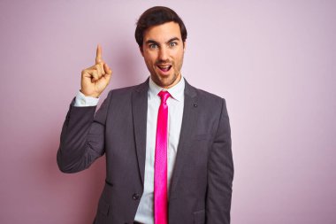 Soyutlanmış pembe arka planda duran takım elbiseli ve kravatlı genç yakışıklı işadamı başarılı bir fikri işaret ediyor. Heyecanlı ve mutlu. Bir numara..