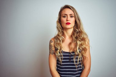 İzole edilmiş beyaz arka plan üzerinde duran çizgili tişört giyen genç ve güzel bir kadın yüzünde ciddi bir ifadeyle rahatlamış. Basit ve doğal bir şekilde kameraya bakıyorsun..