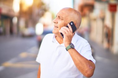 Kıdemli yakışıklı adam mutlu ve kendinden emin gülümsüyor. Yüzünde gülümsemeyle kasaba caddesinde telefonla konuşuyor.