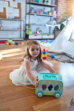 Anaokulunda bir sürü oyuncağın etrafında arabayla oynayan sevimli sarışın çocuk.