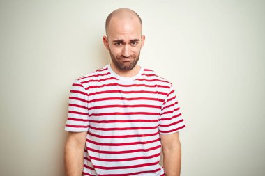 Sakallı, beyaz izole edilmiş arka plan üzerine normal çizgili kırmızı tişört giyen genç kel bir adam depresif ve endişeli, sinirli ve korkmuş. Üzücü ifade.