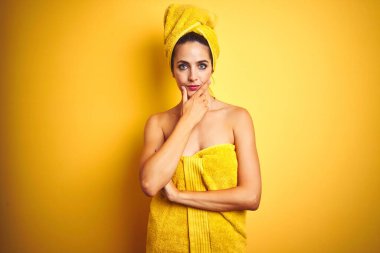 Vücuduna ve başına duş havlusu takmış güzel bir kadın izole edilmiş sarı arka planda kameraya kollarını kavuşturup gülümseyerek ve çenesini kaldırarak bakıyor. Olumlu düşünüyorum..