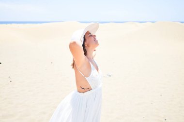 Kollarını açmış güneşlenen genç ve güzel bir kadın yaz tatilinin tadını çıkarıyor.