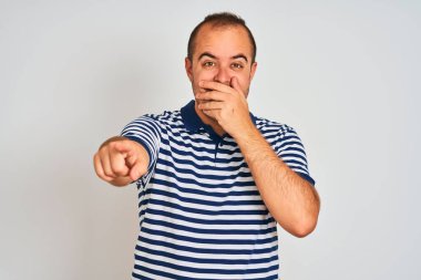 Sıradan çizgili polo giyen genç bir adam izole edilmiş beyaz arka planda durup sana gülüyor, kamerayı işaret ediyor, ağzının üzerinde utanç ifadesi var.