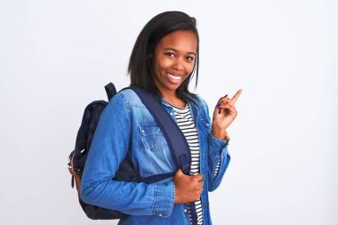 Sırt çantası takan genç Afrikalı Amerikalı bir bayan izole edilmiş arka planda çok mutlu bir şekilde el ve parmak uçlarını işaret ediyor.