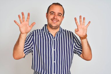 Mavi çizgili gömlekli genç adam izole edilmiş beyaz arka planda dikiliyor ve dokuz numaralı parmaklarıyla işaret ederken kendinden emin ve mutlu bir şekilde gülümsüyor..