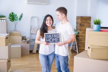 Karton kutular etrafında yeni evde mesaj ile kara tahta tutan katta duran genç güzel çift