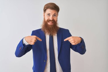 İzole edilmiş beyaz arka planda duran takım elbiseli genç kızıl saçlı işadamı yüzünde bir gülümsemeyle gururlu ve mutlu bir şekilde kendini işaret ediyor..