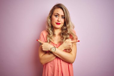 Pembe izole edilmiş arka planda duran tişört giyen genç ve güzel bir kadın. İki tarafı da parmaklarıyla işaret ediyor. Farklı yönler farklı.