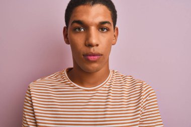 Çizgili tişört giyen genç yakışıklı Arap adam izole edilmiş pembe arka planda dikiliyor ve akıllı yüz ifadesiyle ciddi ciddi düşünüyor.