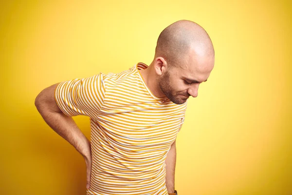 黄色の隔離された背景の上にカジュアルなストライプのTシャツを身に着けているひげを生やして若いはげ男腰痛の苦しみ 手で背中に触れる 筋肉痛 — ストック写真