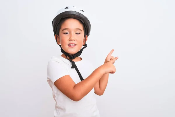Beautiful kid boy wearing bike security helmet standing over isolated white background smiling and looking at the camera pointing with two hands and fingers to the side.