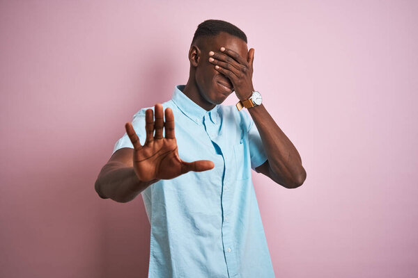 African american man wearing blue casual shirt standing over isolated pink background covering eyes with hands and doing stop gesture with sad and fear expression. Embarrassed and negative concept.
