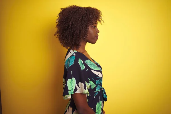 若いですアフリカ人女性身に着けています夏の花のドレス上の隔離された黄色の背景見ます側 リラックスしたプロフィールポーズとともに自然な顔と自信笑顔 — ストック写真