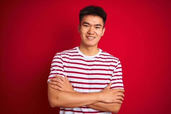 縞模様のTシャツを着た若いアジア系中国人男性が カメラを見ている両腕を組んで笑顔で赤い背景に立っている 正の人 — ストック写真