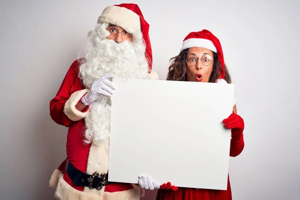 上了年纪的夫妇 身穿圣诞老人的服装 举着横幅遮掩在孤独的白色背景上 吓得满脸诧异 吓得面无血色 吓得面无血色 — 图库照片