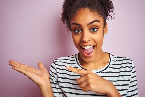 Siyah çizgili tişört giyen Afro-Amerikalı kadın izole edilmiş pembe arka planda el ve parmak göstererek mutlu bir şekilde duruyordu.