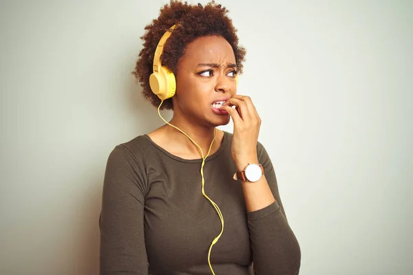 African american woman wearing headphones listening to music over isolated background looking stressed and nervous with hands on mouth biting nails. Anxiety problem.