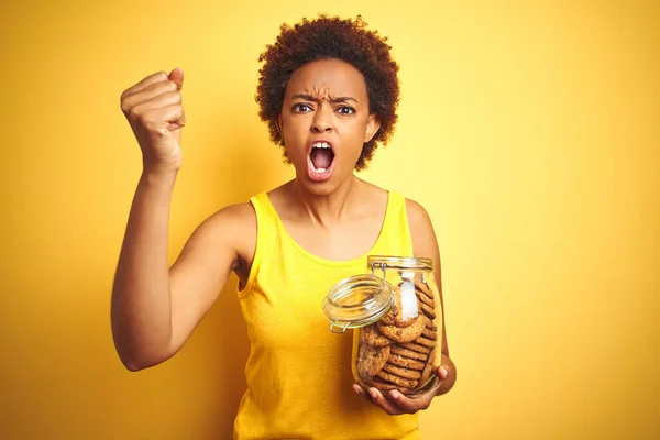 アフリカ系アメリカ人女性を保持Jarのチョコレートチップクッキー上の黄色の背景不満と不満怒りと叫びます クレイジーと大声で手を上げと 怒りの概念 — ストック写真